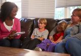 Social worker holding a clipboard, sat on sofa with mother and two children