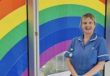 Sharon Maywood stood in blue nurses' uniform with a rainbow background
